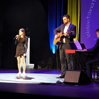Wokalistka, mężczyzna z gitarą i klawiszowiec wykonują na scenie utwór
