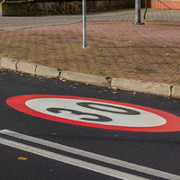 Namalowany na drodze okrągły znak z czerwoną obwódką, białym środkiem i czarną liczbą 30