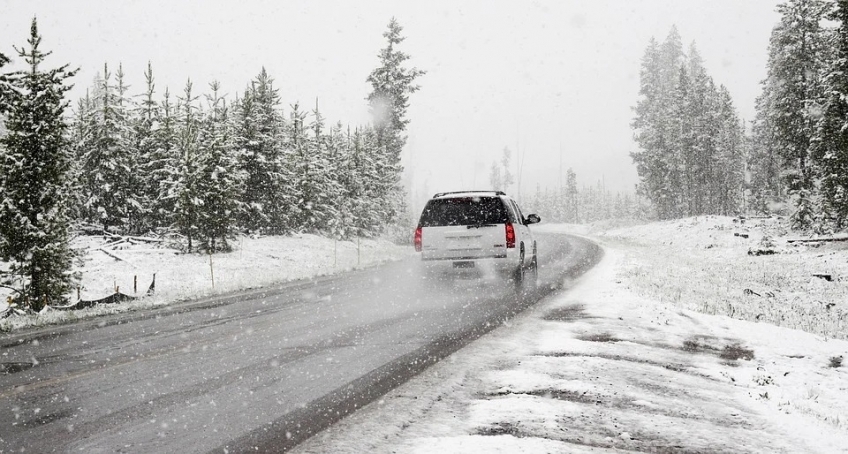 zdjęcie przedstawia jadący samochód na drodze asfaltowej podczas gdy pada śnieg